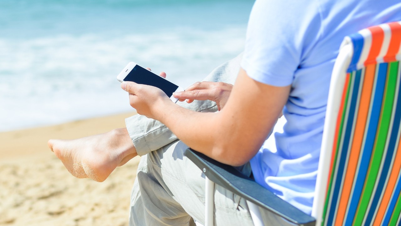 A man sitting on the beach with his mobile phone; image used for HSBC India Mobile banking page.