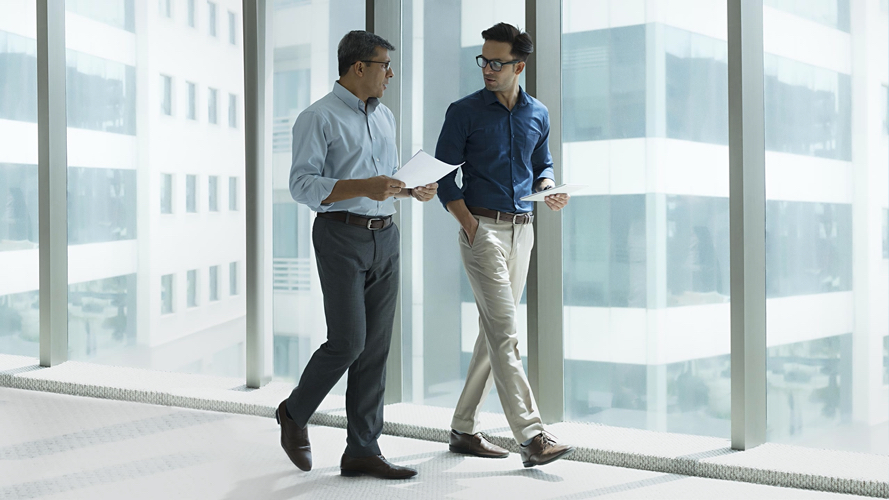 Two men walking along office corridor with floor to ceiling windows